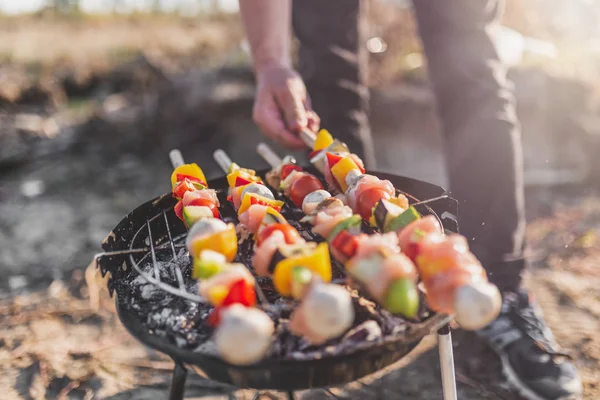 Man hand turning meat and vegetables while grilling on barbecue. Picnic or camping food concept.