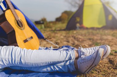 Genç bir bayan, arka planda akustik gitar ve çadır eşliğinde kamp yapmaktan hoşlanıyor. Kopyalamak için boşluk.