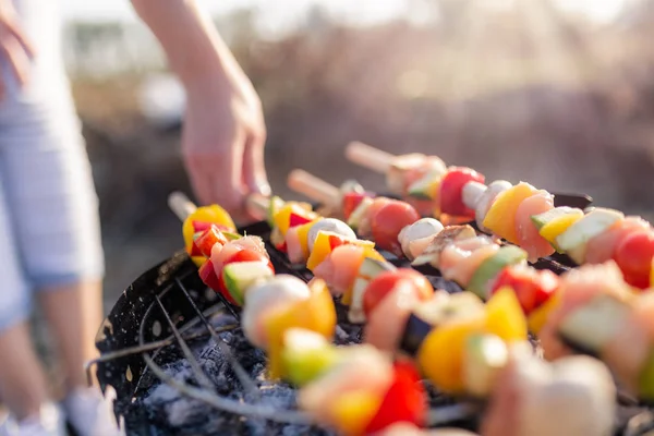 Femme main tourner la viande et les légumes tout en grillant sur le barbecue. Concept de pique-nique ou camping . — Photo