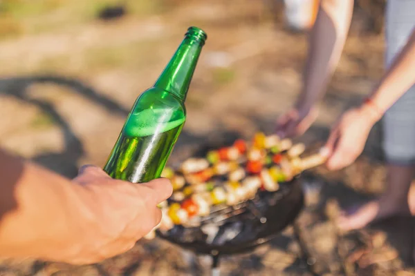 Amigos tomando cerveza y preparando el almuerzo con carne y verduras en la parrilla de barbacoa al aire libre . — Foto de Stock