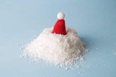 Kar yığını ve pastel mavi arka plana karşı kırmızı Noel şapkası. En az yaratıcı kış mevsimi konsepti..
