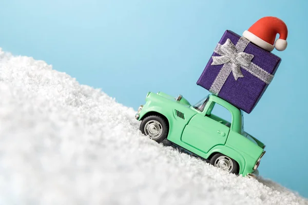 Hediye kutulu eski araba oyuncağı ve Noel Baba şapkası karlı dağlarda minimum yaratıcı kış tatili konseptine çıkıyor.. — Stok fotoğraf