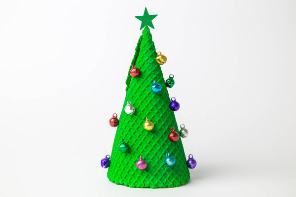 Christmas tree abstract made of ice cream cone and miniature multicolored baubles with star on white.