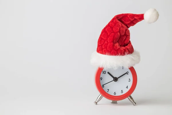 Red alarm clock wearing Santa hat against white background minimal creative christmas holiday concept. Space for copy. — Stock Photo, Image