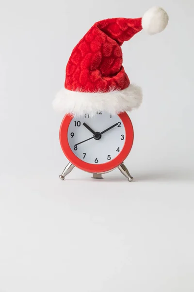 Red alarm clock wearing Santa hat against white background minimal creative christmas holiday concept. Space for copy. — Stock Photo, Image