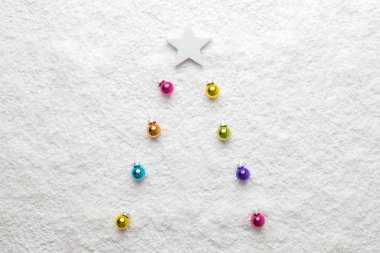 Christmas background abstract made of multicolored decoration baubles as fir tree and white star in snow.