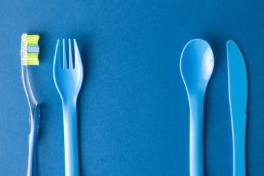 Plastik çatal, kaşık ve bıçak mavi arka planda diş fırçası ve ağız temizliği soyut.