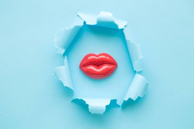 Dişi plastik dudakların patlaması mavi arka planda soyut.