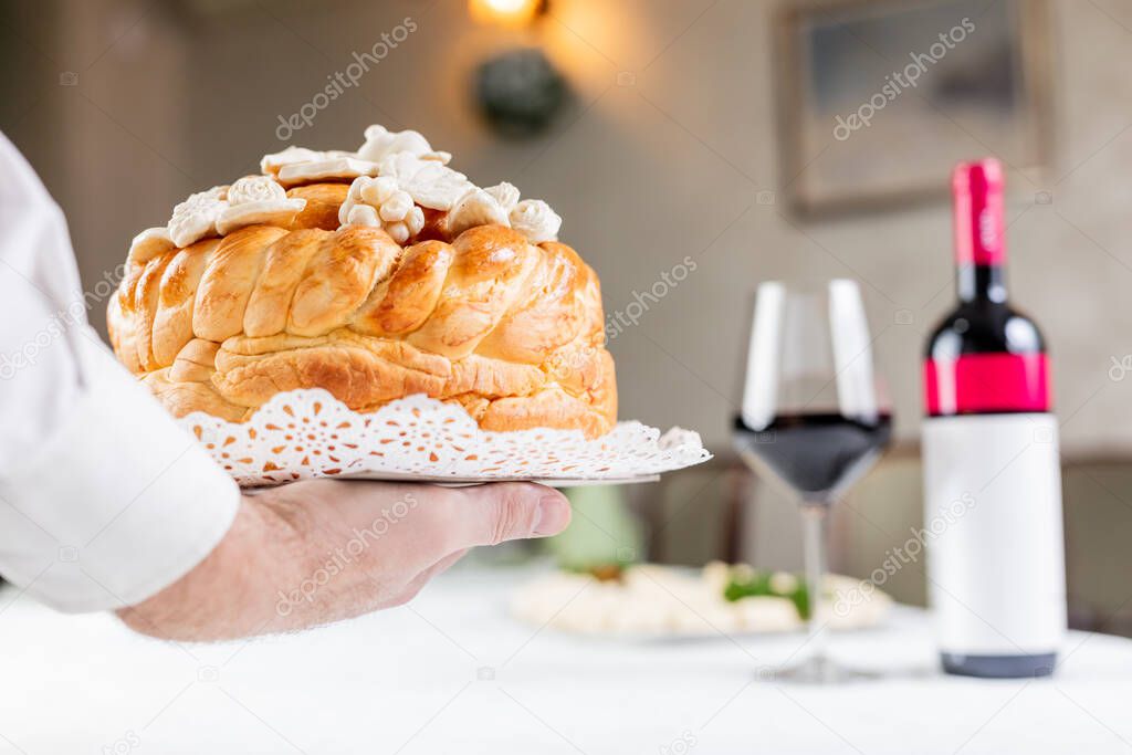 Close up of hand holding traditional orthodox bread next to wine at the table.