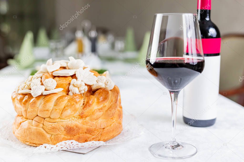 Bottle and glass of wine and Orthodox church bread with decoration on table at restaurant or home.