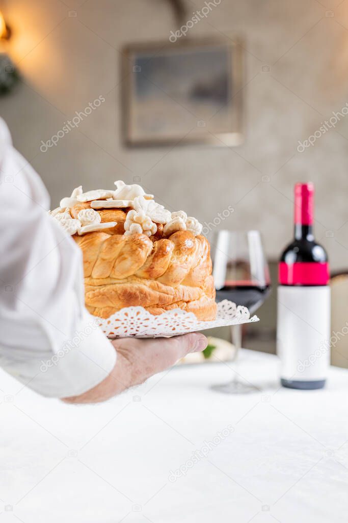 Close up of hand holding traditional orthodox bread next to wine at the table.