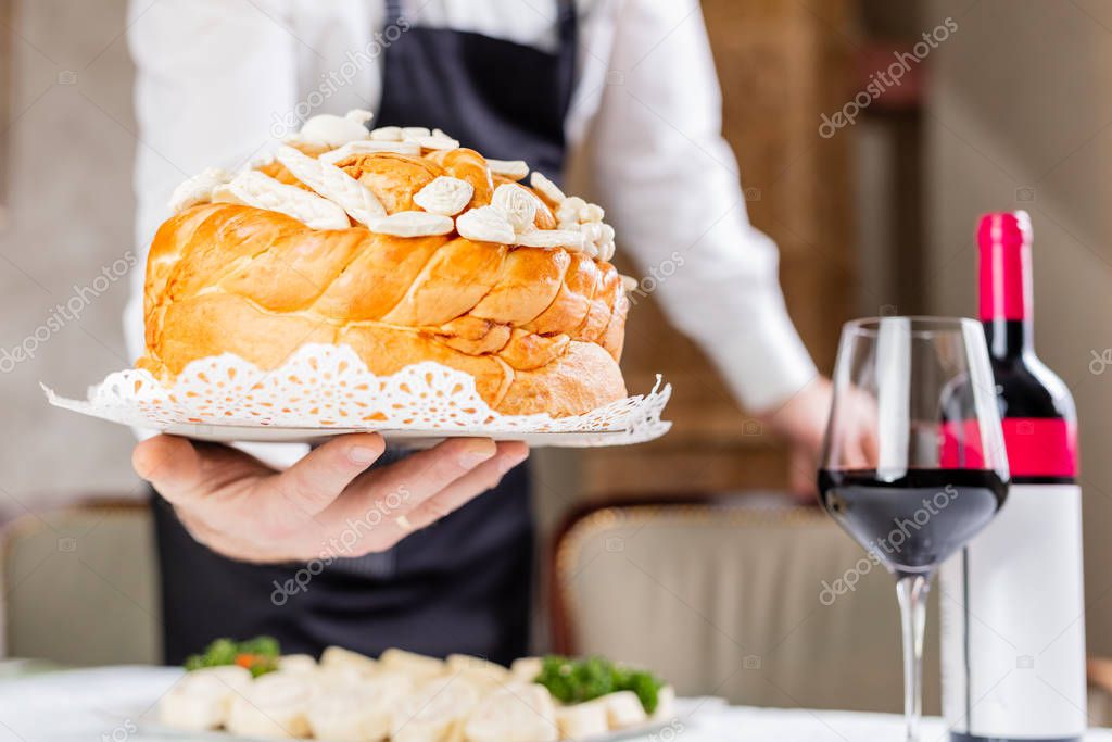 Man hand bringing orthodox homemade bread at the table with glass and bottle of wine in the background.