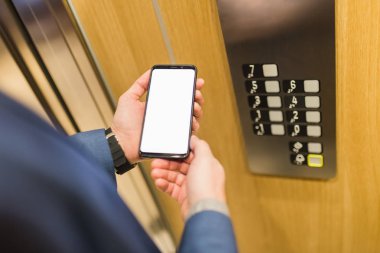 Asansör kontrol panelinin yanında boş cep telefonu tutan bir adam elleri var..