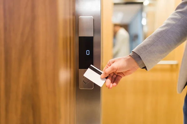Man holding key card on sensor to open elevator door in modern building or hotel.