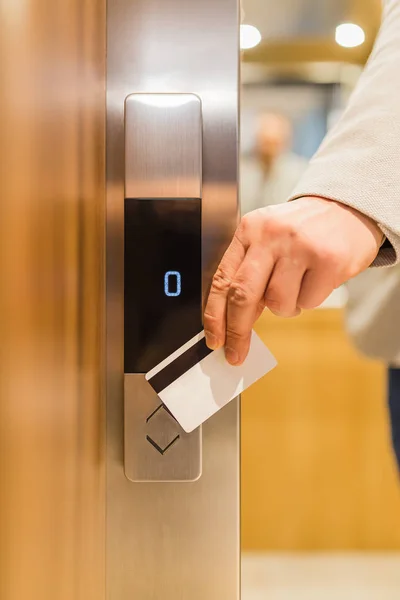 Άνδρας που κρατά κάρτα-κλειδί στον αισθητήρα για να ανοίξει την πόρτα του ανελκυστήρα στο σύγχρονο κτίριο ή ξενοδοχείο. — Φωτογραφία Αρχείου