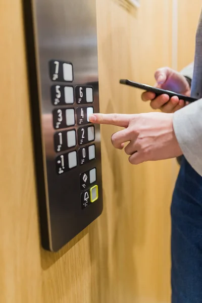 Чоловік тримає мобільний телефон під час використання панелі керування ліфтом . — стокове фото