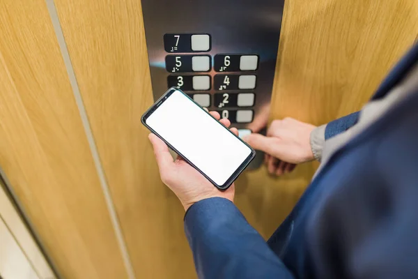 Mãos de homem segurando o telefone celular da tela em branco ao usar o painel de controle do elevador . — Fotografia de Stock