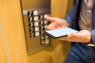 Asansör kontrol paneli kullanırken elleri boş cep telefonu tutan bir adam..