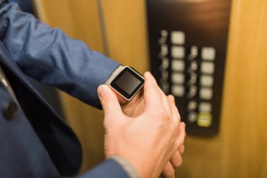 Asansördeki boş ekran akıllı saate bakan işadamlarına yaklaş. İş ve ofis binaları toplantısı konsepti.