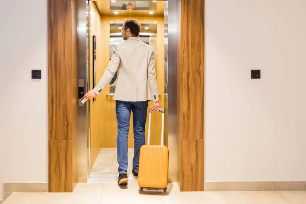 Modern businessman entering the elevator with luggage. Business and travel concept.