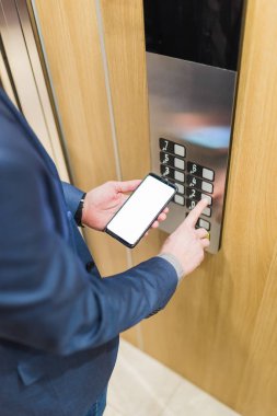 Asansör kontrol paneli kullanırken elleri boş cep telefonu tutan bir adam..