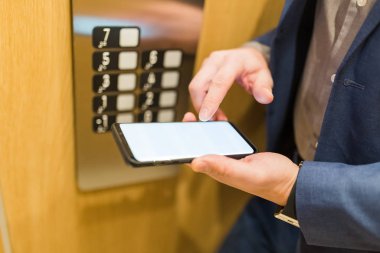Asansör kontrol panelinin yanındaki boş ekran akıllı telefonu kullanarak iş adamını kapat. İş ve ofis binaları toplantısı konsepti.