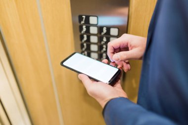 Asansör kontrol panelinin yanında boş cep telefonu tutan bir adam elleri var..