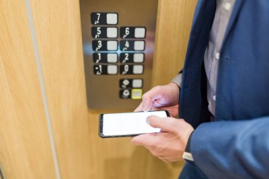 Asansördeki işadamı kontrol panelinin yanında boş ekran akıllı telefonu tutuyor..