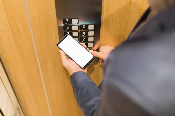 エレベーターコントロールパネルの床ボタンを押しながら 空白の画面携帯電話を保持男の手 — ストック写真