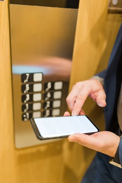 Close up of businessman using blank screen smartphone in elevator. Business and office building meeting concept.