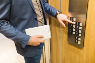 Asansör düğmesine basılı tablet cihazlı işadamını kapat. İş ve ofis binaları toplantısı konsepti.