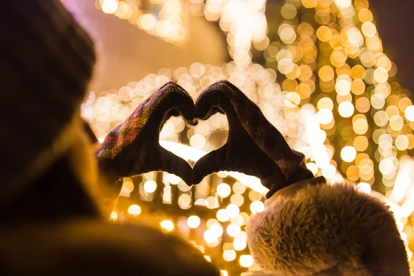 ハートの形をした手袋をしている女性の手 背景にボケクリスマスの新年の装飾 — ストック写真