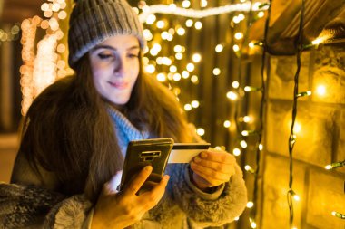 Sokakta akıllı telefon ve kredi kartı kullanan ve yeni yıl hediyesini hazırlayan bir kadın alıcı..