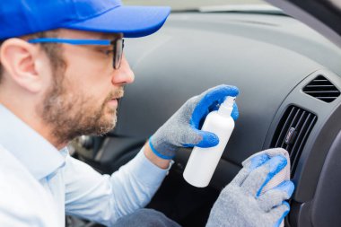 Aracın içini temizlemek için dezenfektan ve mikrofiber bez kullanan profesyonel bir işçi..