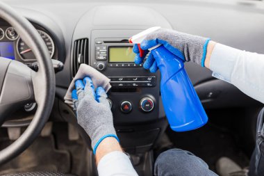 Arabanın içini temizlerken insan ellerini mikrofiber bez ve sprey kullanarak kapat..