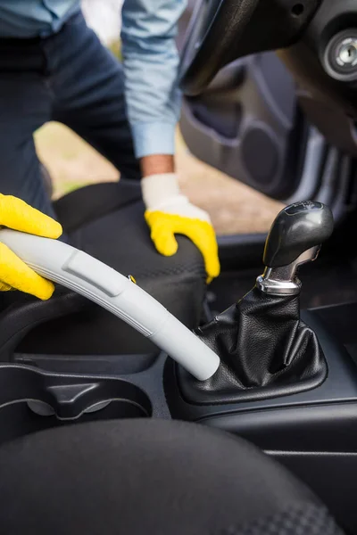 Close up of car wash service worker with protective gloves cleaning car interior with vacuum cleaner.