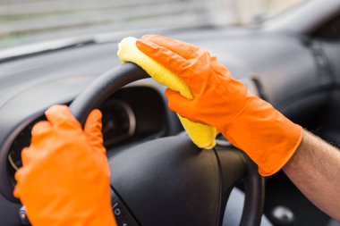 Eller koruyucu eldivenlerle arabanın direksiyonunu mikrofiber bezle temizler..