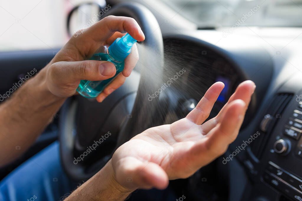 Man hands spraying disinfectant in car interior, coronavirus prevention concept.