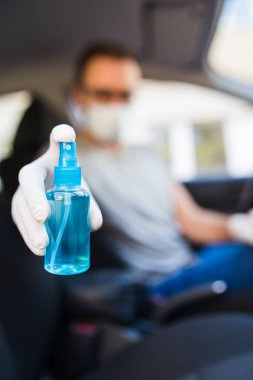 Koruyucu maskeli, elinde alkol dezenfektanı tutan lastik eldivenler takan, bakteri ve virüs enfeksiyonundan korunan bir adam. Arabanın içi..