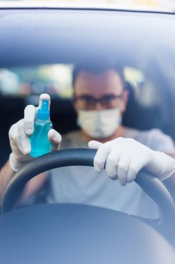 Koruyucu maske takan, direksiyonda lastik eldiven takan, elinde alkol dezenfektanı tutan, bakteri ve virüs enfeksiyonundan korunan, koruyucu maskeli sürücüyü kapat..