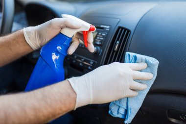 Arabanın içini temizlerken insan ellerini mikrofiber bez ve sprey kullanarak kapat..