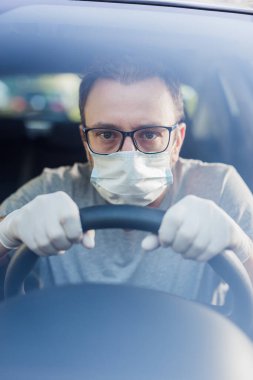 Koruyucu maskeli, elleri lastik eldivenli, direksiyonlu, bakteri ve virüs enfeksiyonundan korunan sürücüyü kapatın..