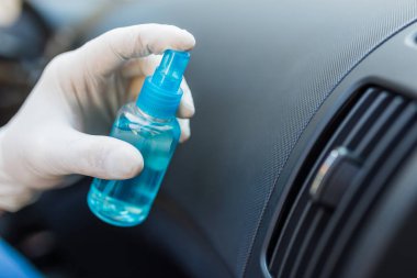 Elinde dezenfektan tutan ve araba havalandırmasını spreyleyen lastik eldivenlerle ellerini kapat..