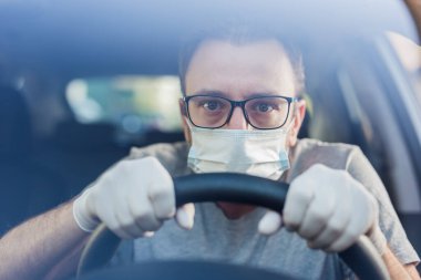 Koruyucu maskeli, elleri lastik eldivenli, direksiyonlu, bakteri ve virüs enfeksiyonundan korunan sürücüyü kapatın..