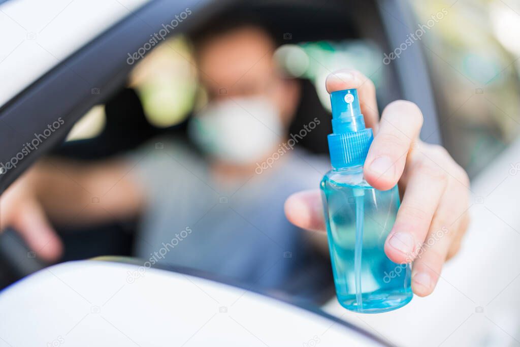 Portrait of man with surgical mask sitting in car and holding sprayer sanitizer. Hygiene concept.