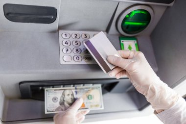 Yüz dolarlık banknotlar tutan ve ATM 'de kredi kartı kullanan eller. Covid-19 konsepti.
