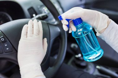 Araba direksiyonunu bakterilerden korumak için sprey şişe dezenfektanı kullanan lastik eldivenli eller. Antiseptik, hijyen ve sağlık konsepti.