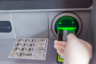 Kadın elinin koruyucu ameliyat eldiveni giyip ATM 'ye kredi kartı koymasını. Coronavirus konsepti.