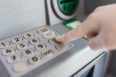 Koruyucu tıbbi eldiven giyip ATM 'den kredi kartı şifresini girerken yakın plan. Coronavirus önleme kavramı.