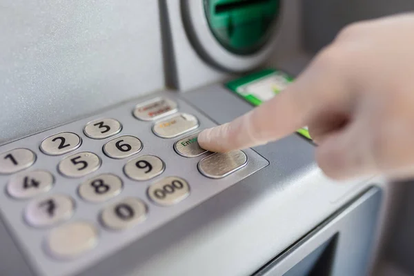 Close up of hand wearing protective medical glove entering credit card pin code at atm. Coronavirus prevention concept.